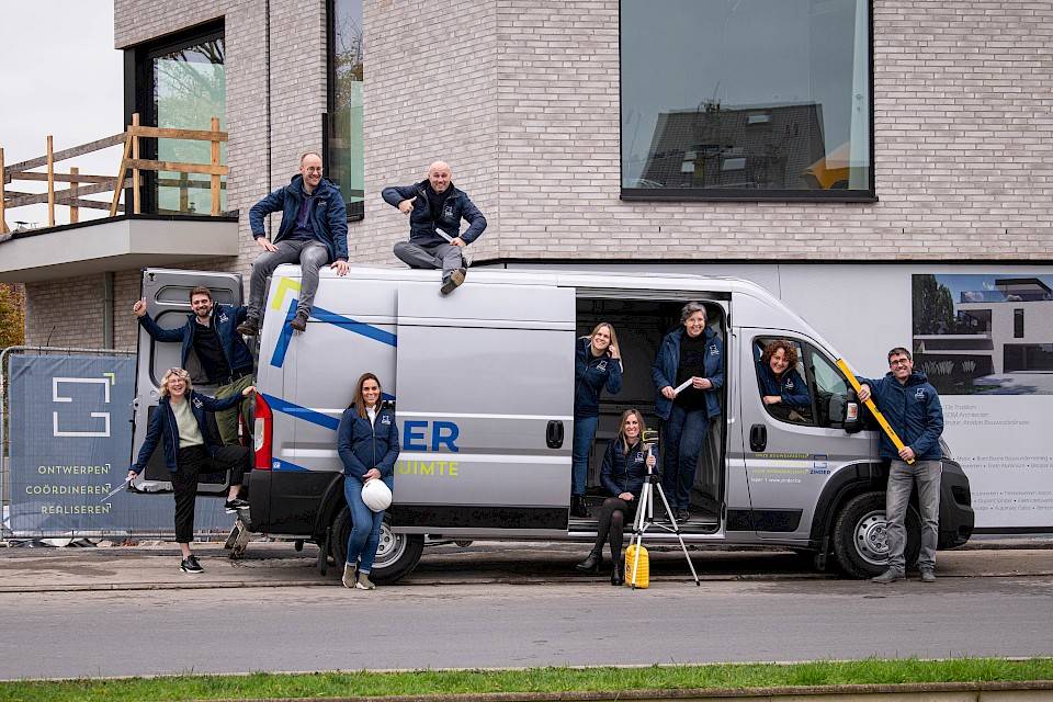Het team van Zinder dat poseert voor hun bestelwagen met op de achtergrond een huis in opbouw.